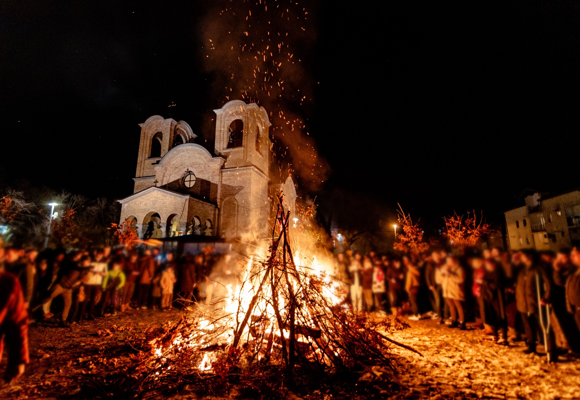 Large bonfire with gathering crowd near a church at night